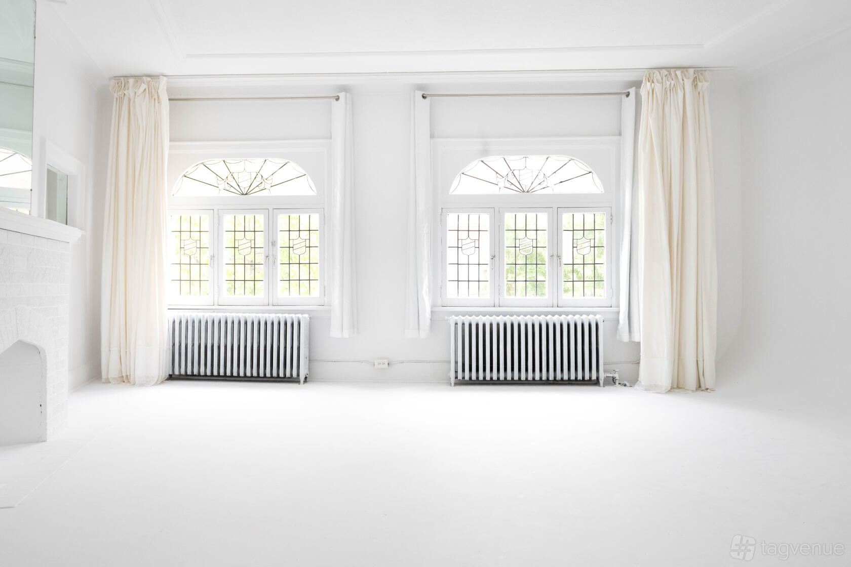 A photo studio with white walls, arched windows with stained glass, and sheer curtains at Studio Buddy Toronto.