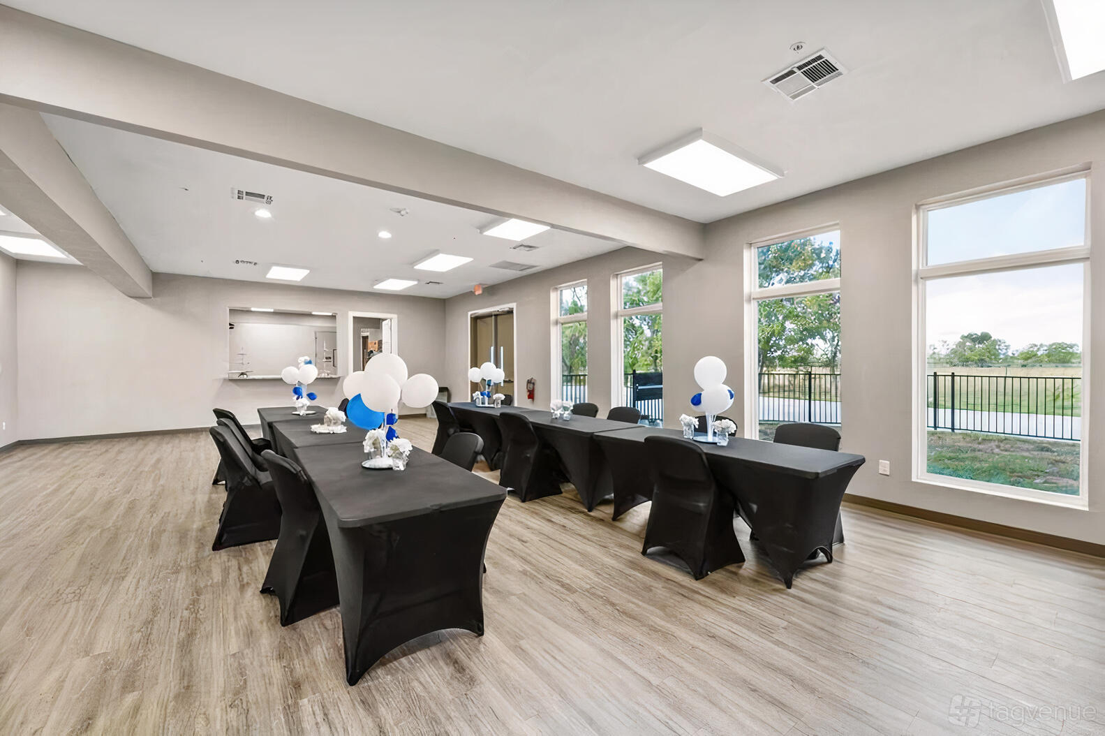 An event venue with large windows, wood-look flooring, and banquet tables with black linens at Manvel Mansion Event Center.