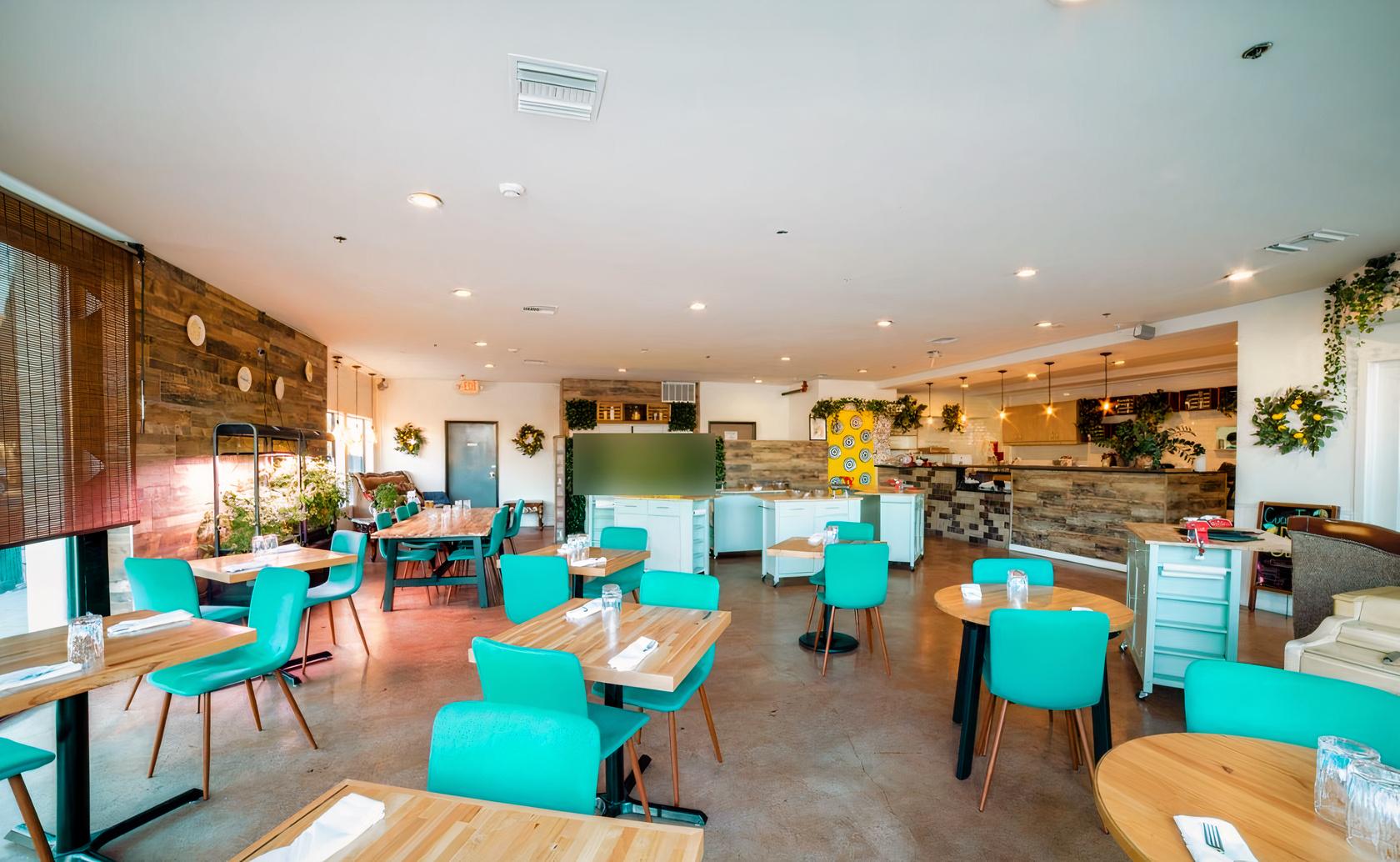 A restaurant with teal chairs, light wooden tables, and rustic wood accent walls at Mattarello Cooking Lab.