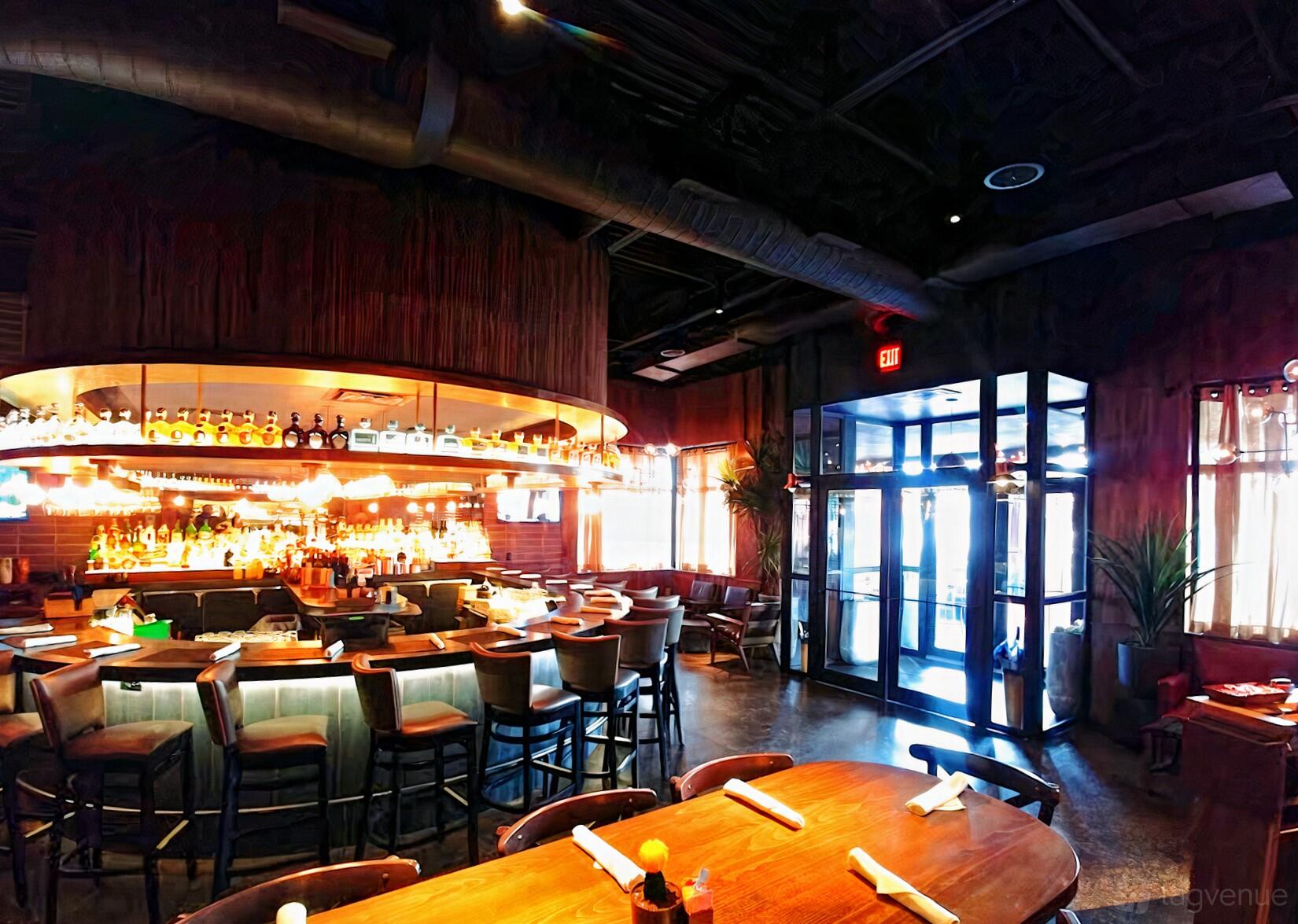 A restaurant with a circular bar, backlit shelves of liquor, and wood tables at Meso Maya - Lakewood.