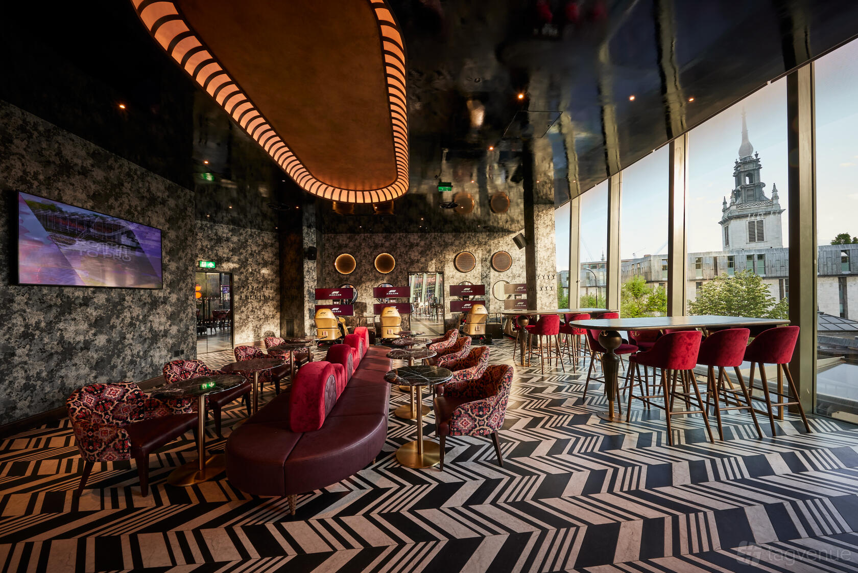 A function room with patterned flooring, velvet seating, floor-to-ceiling windows, and city views at F1 Arcade, St Pauls, London.