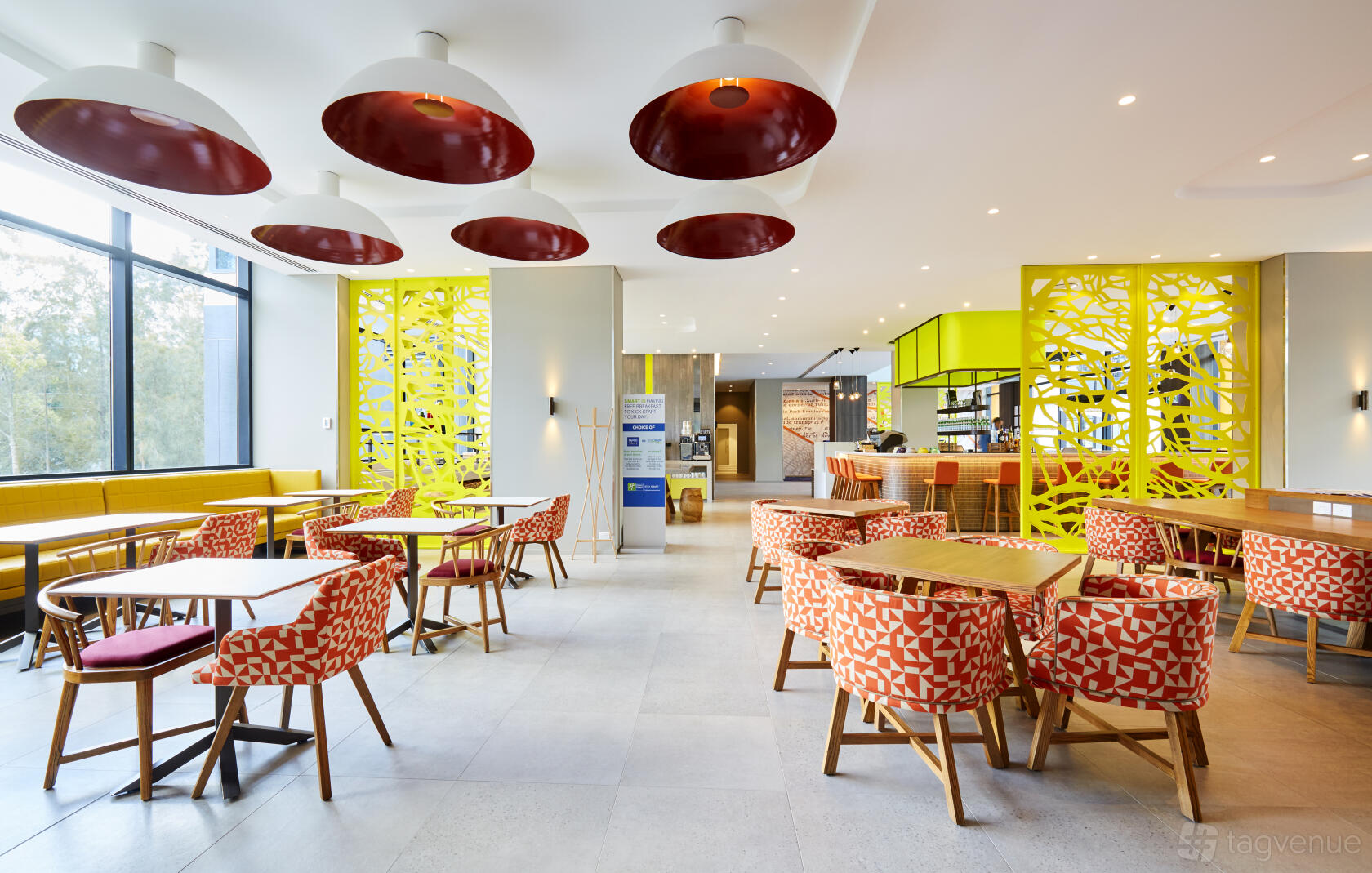 An event space in a hotel with geometric-patterned chairs, round tables, and bright yellow accent walls at Holiday Inn Express Sydney Macquarie Park.