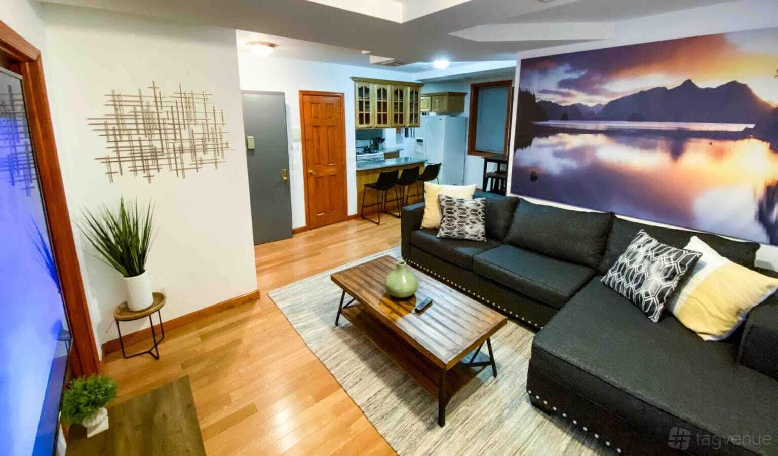 A country house living area with wooden floors, sectional sofa, wall art, and an open kitchen at Z studio 39th Avenue.