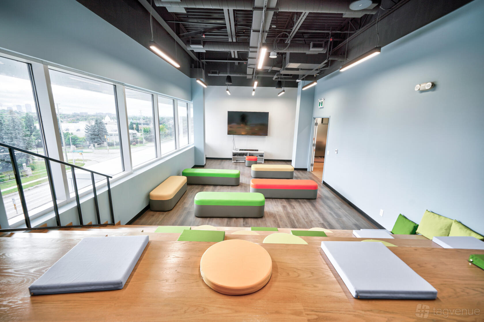 A meeting room with tiered wooden seating, colorful benches, and large windows at LaunchHub Space.