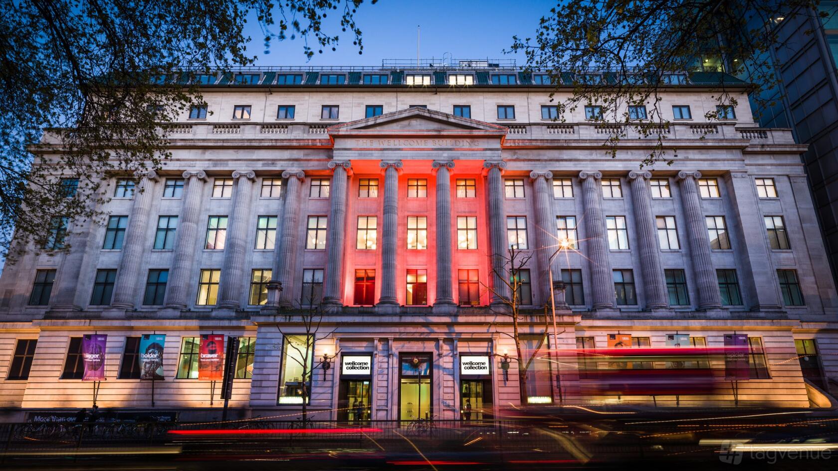 A historic conference centre with grand columns, lit-up façade, and large windows at Wellcome Collection.