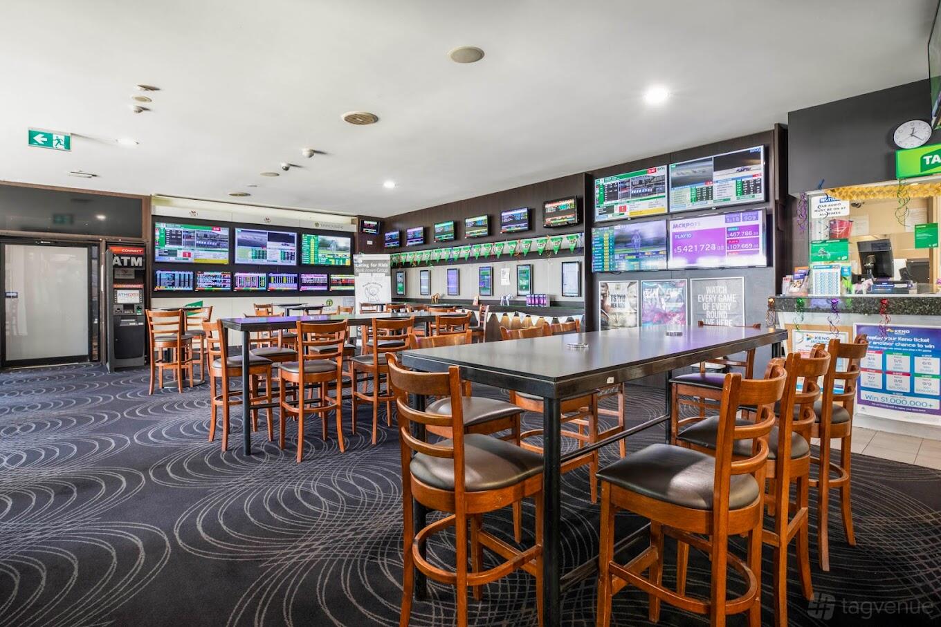 A pub with multiple wall-mounted screens, high tables with wooden chairs, and patterned carpeting at The High Flyer.