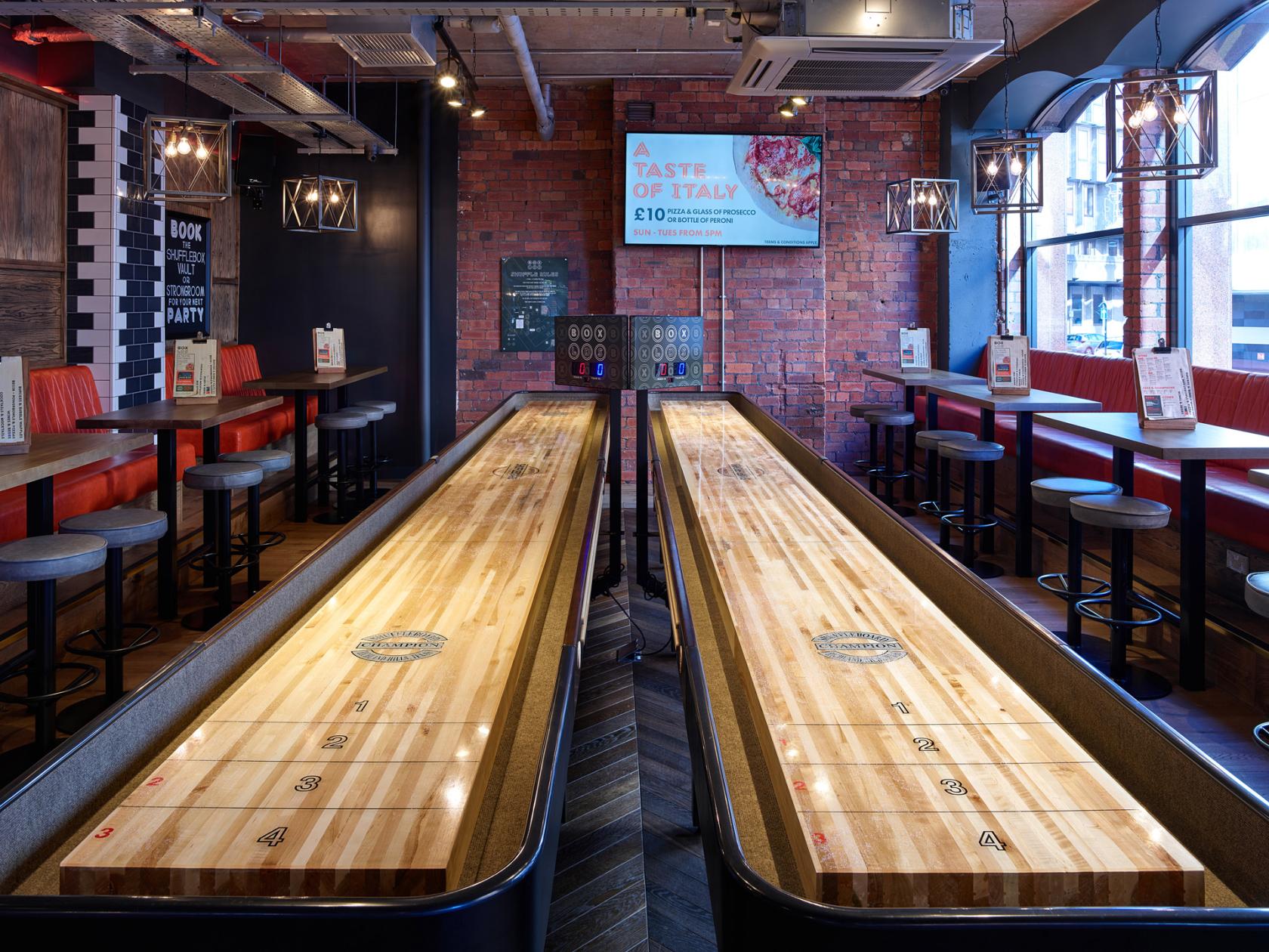 An event space with shuffleboard tables, exposed brick walls, and high seating at Box Leeds.