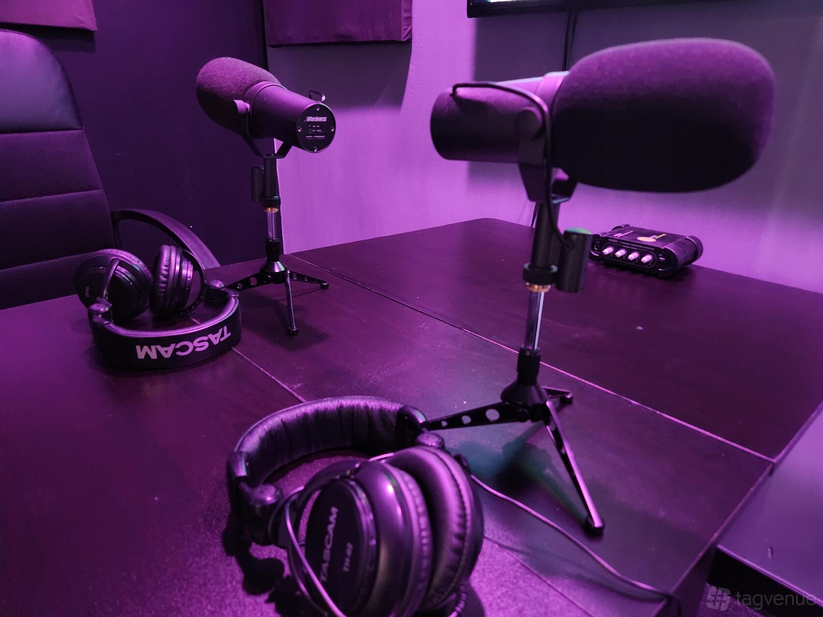 A podcast studio with tabletop microphones, headphones, and a black recording desk at Cave Rec Studio.