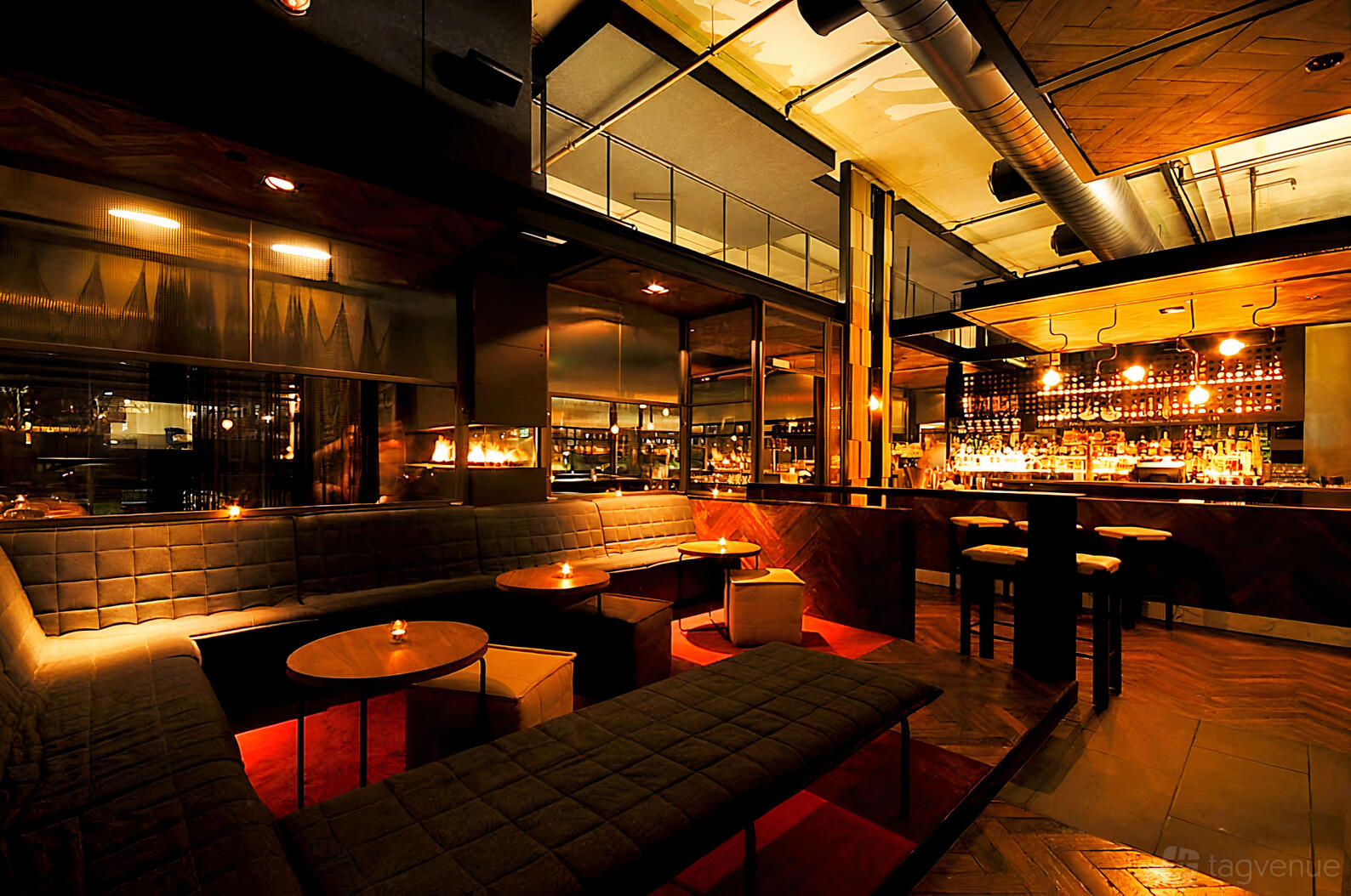 A lounge in a pub with black tufted banquettes, round wooden tables, and warm ambient lighting at Ludlow Bar.