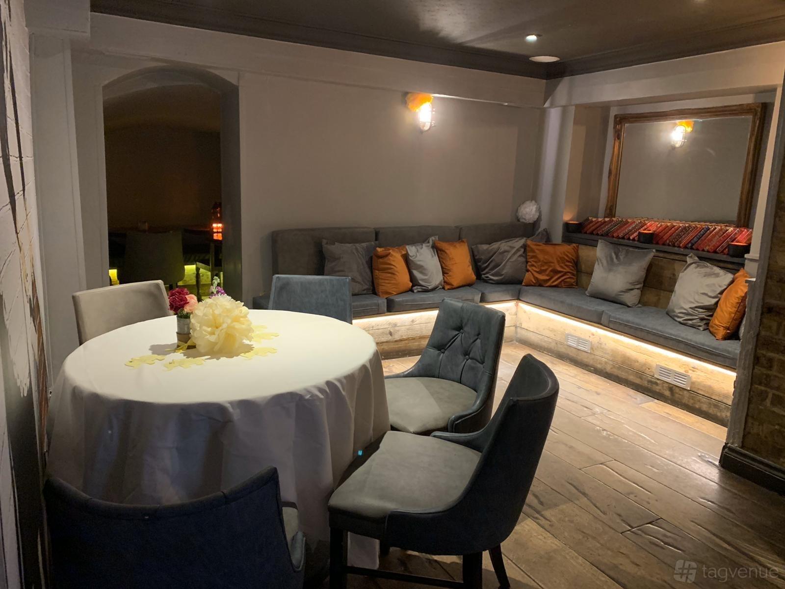 An event space in a pub with a round table draped in white linen and cushioned banquette seating at The Princess of Wales.