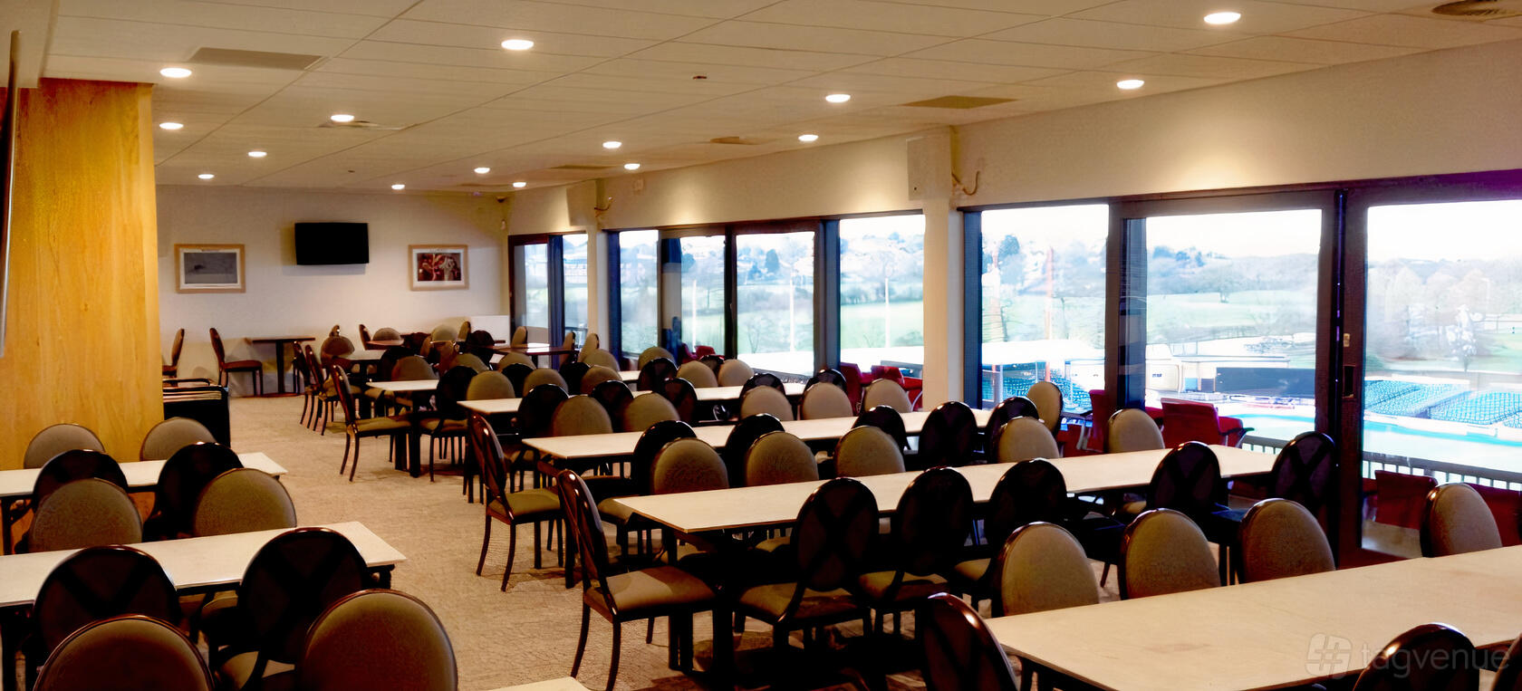 A stadium lounge with rows of oval-backed chairs, rectangular tables, and floor-to-ceiling windows at StoneX Stadium.