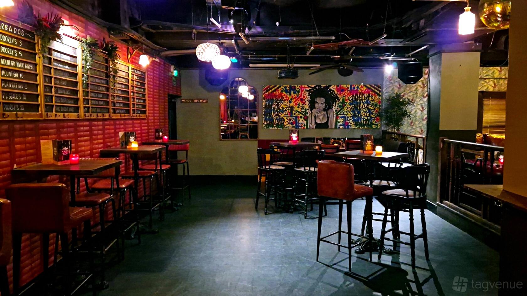 A cocktail bar with high tables, exposed brick walls, colorful artwork, and pendant lighting at Burlock Rum Room.