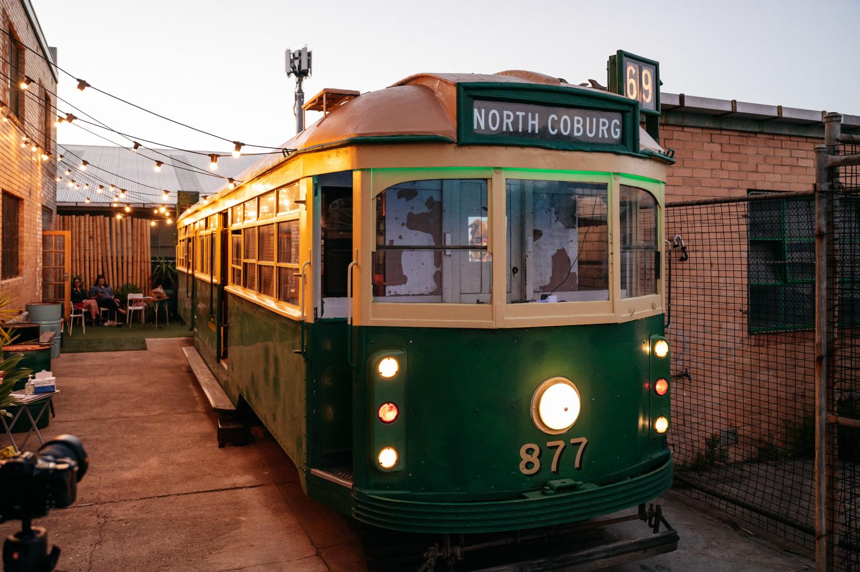 A warehouse with an outdoor courtyard featuring a vintage green tram and string lights at Bighouse Arts.
