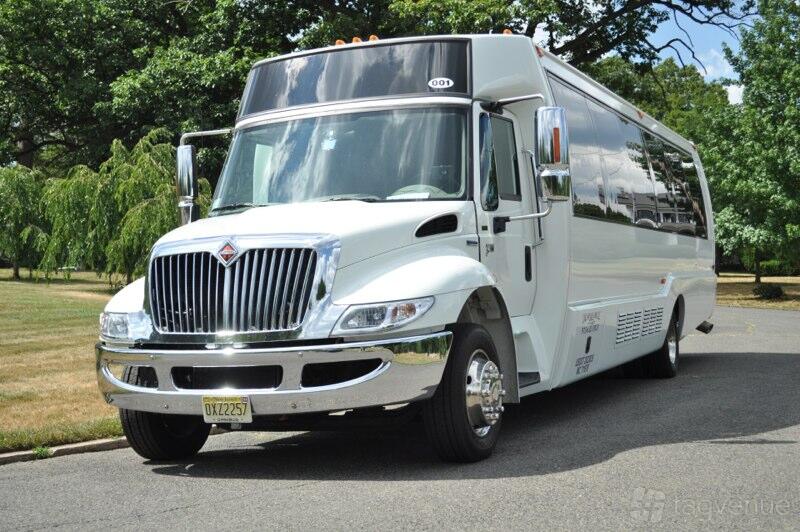 A white party bus with tinted windows and chrome trim parked on a tree-lined street at US Bargain Limo.