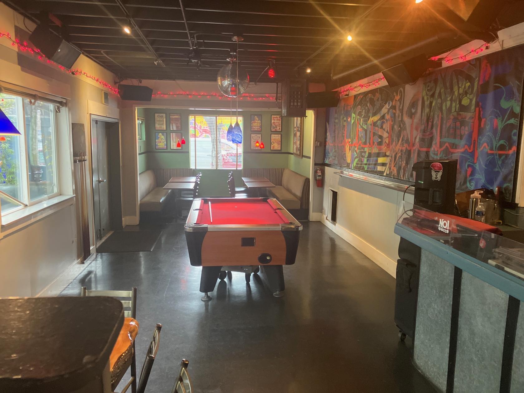 A bar with a red-felt pool table, booth seating, artwork on the walls, and a disco ball at Mars Bar Restaurant.