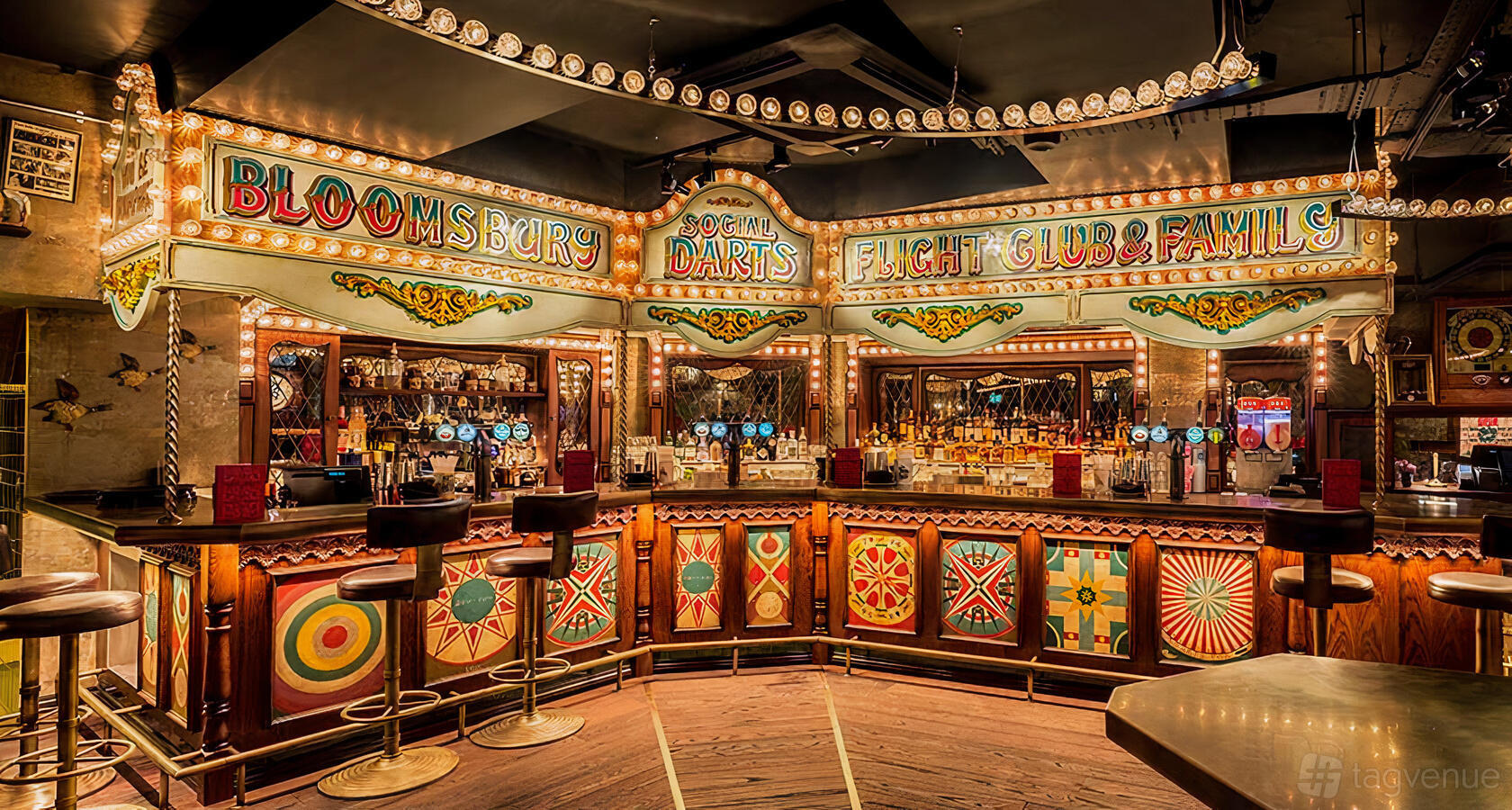 A dining room in a bar with carnival-inspired decor, illuminated signs, and a dartboard at Flight Club Bloomsbury.