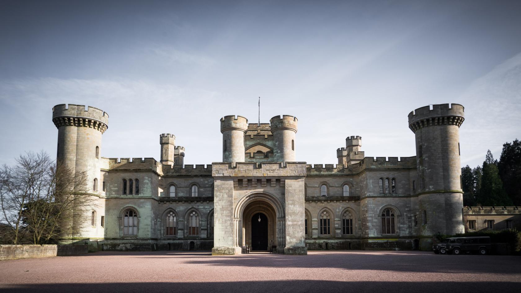 A historic castle with stone towers, arched entrance, and symmetrical turrets at Eastnor Castle.