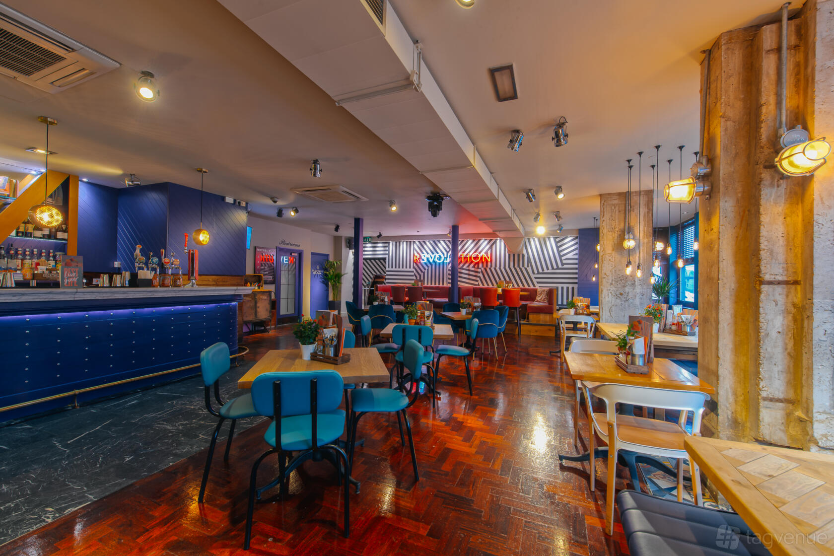 A bar with colorful seating, parquet floors, neon signage, and exposed columns at Revolution Cambridge.