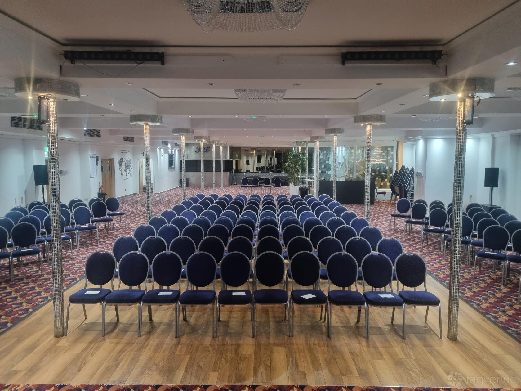 An auditorium with rows of navy cushioned chairs, mirrored columns, and patterned carpet at Potters House.