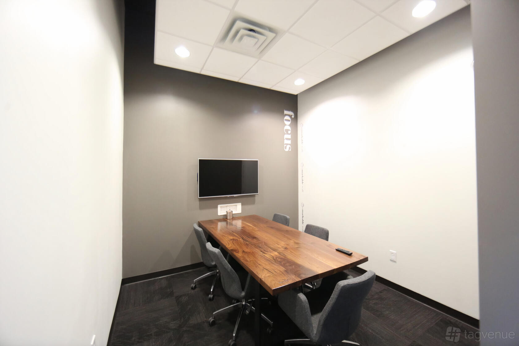 A meeting room with a wooden conference table, four gray chairs, and a wall-mounted TV at ROAM GALLERIA.